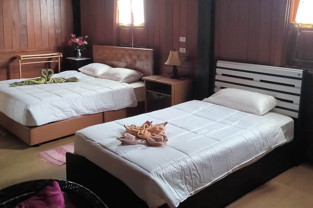 Une chambre avec deux lits, un plafond en bois, une fenêtre avec des rideaux, une table de chevet avec une lampe et une petite table sur laquelle est posé un vase de fleurs.