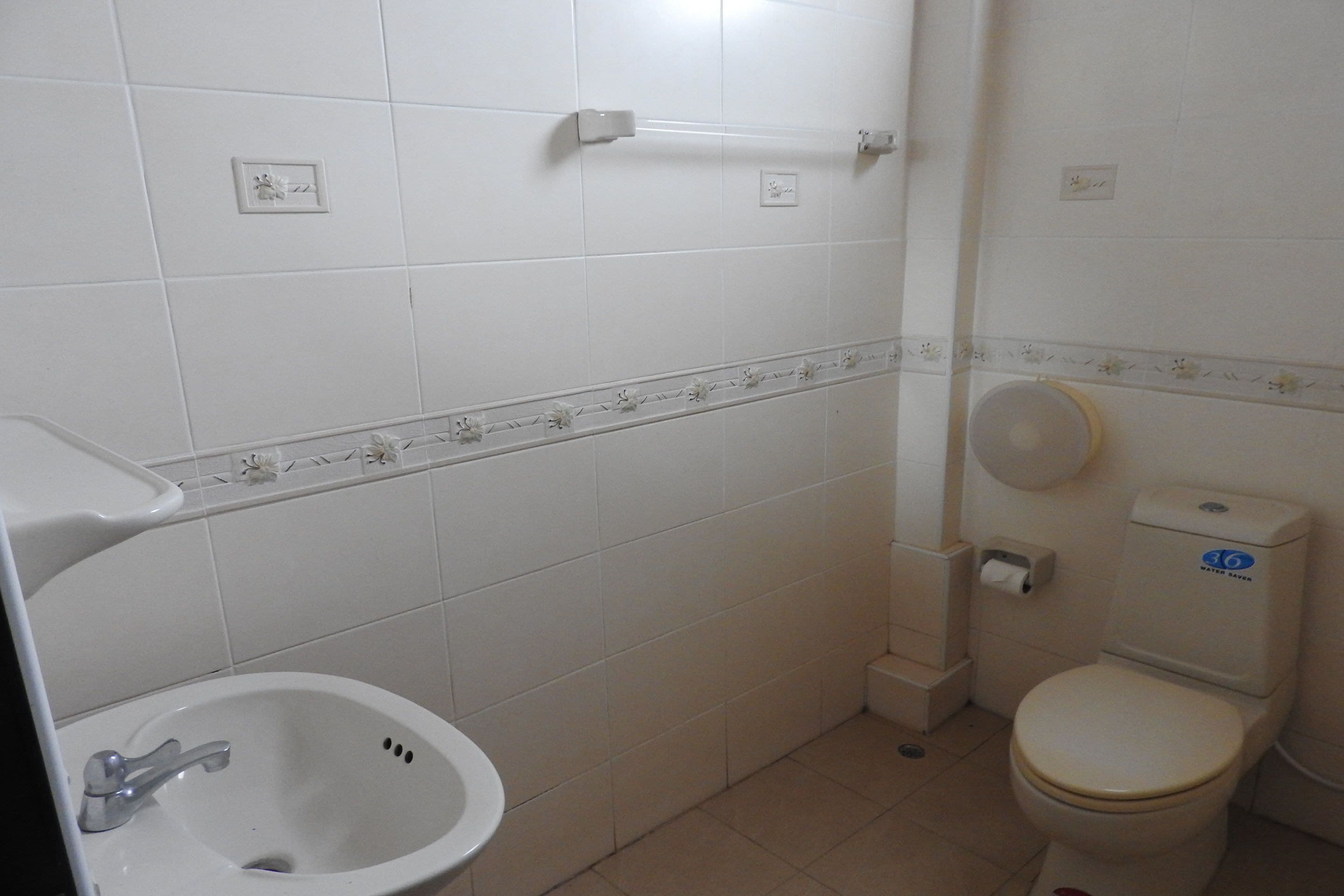 A bathroom with a white sink, toilet, and a small trash bin.