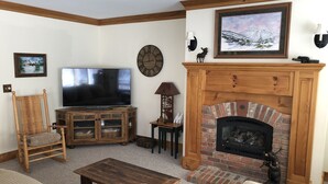 Una sala de estar con chimenea, televisor, un reloj y un cuadro en la pared.