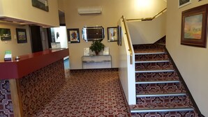Un área de recepción con alfombra estampada, un mostrador de recepción, una escalera con peldaños decorados y obras de arte enmarcadas en las paredes.
