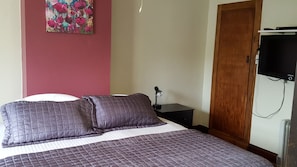 A neatly made bed with a purple quilt, a bedside lamp, and a wall-mounted TV. - Foveaux Hotel (Bluff)