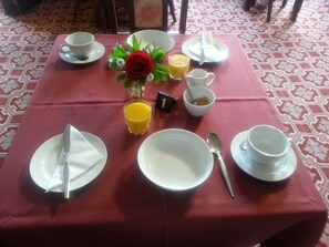 A table set for breakfast with plates, bowls, a glass of orange juice, and a red rose centerpiece. - Foveaux Hotel (Bluff)