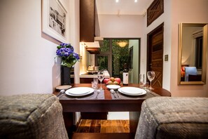 A dining table set for two with a vase of flowers, a bottle of wine, and a fruit bowl. - New Gate Apartment (Hanoi)