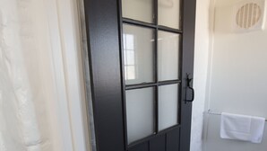 A black door with frosted glass panels, a white towel hanging on a rack, and a stone-tiled floor. - Paxton Square Cottages (Burra)