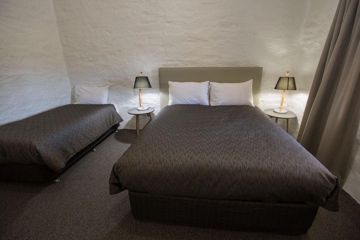 Quarto com duas camas, cada uma com cabeceira e travesseiro combinando, e duas mesas de cabeceira com luminárias.