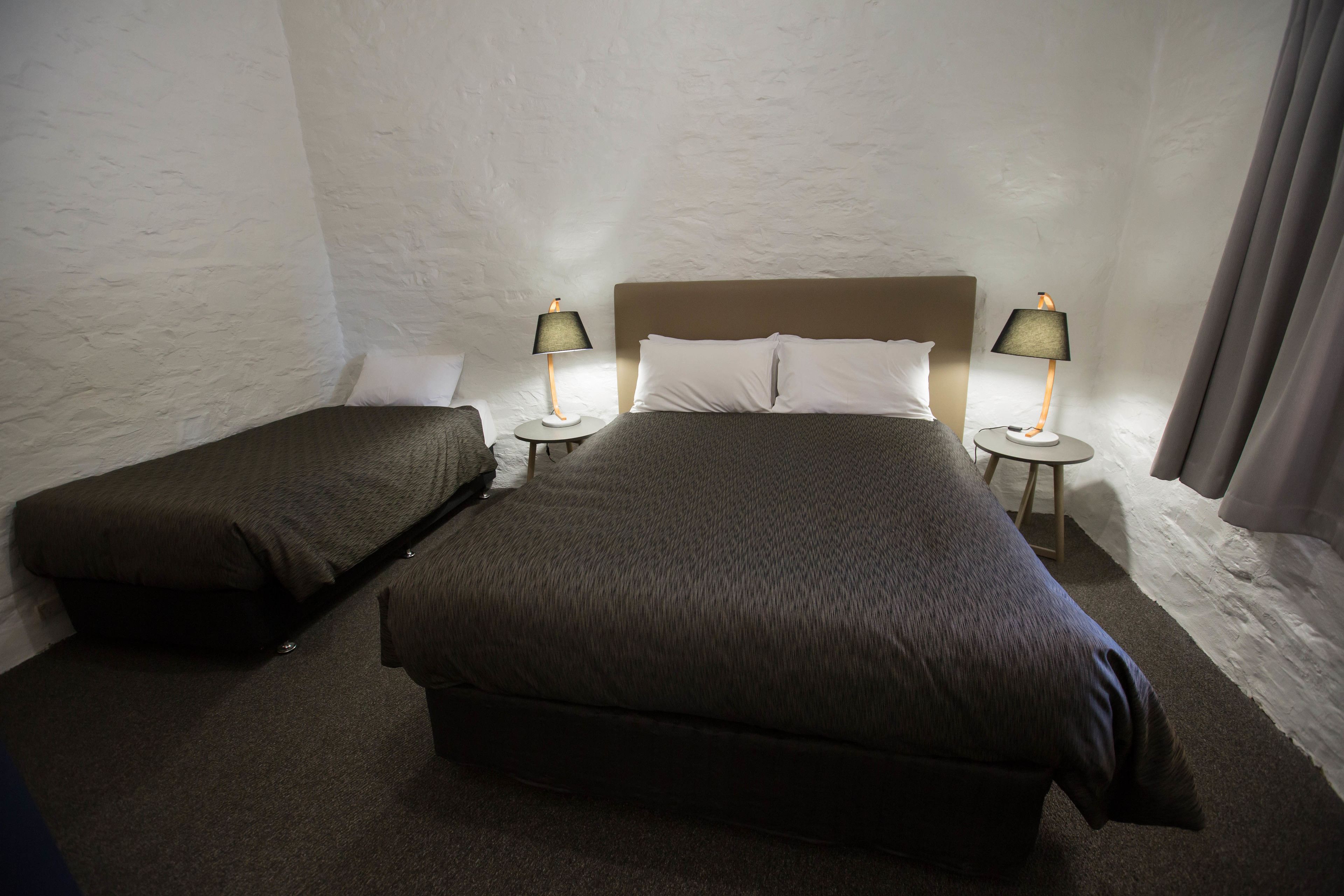 A single bed with a headboard, two bedside tables with lamps, and a small bench.