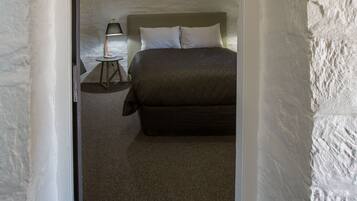 A narrow hallway leading to a bedroom with a bed, a nightstand, and a lamp.
