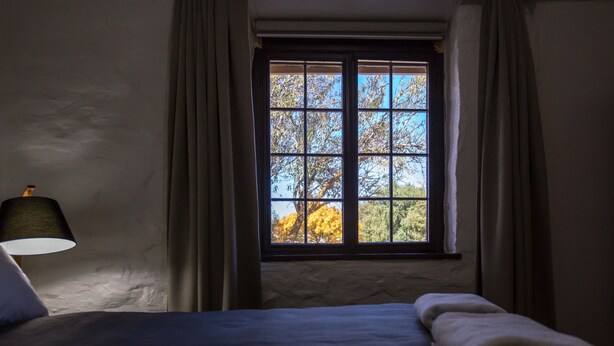 A bedroom with a bed, a window with curtains, and a lamp. - Paxton Square Cottages (Burra)