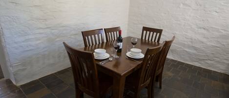 A dining table with four wooden chairs, white plates, glasses, and a bottle of red wine.