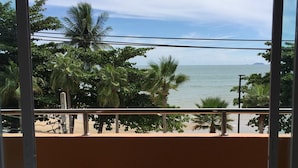 A balcony with two wooden chairs and a small round table, overlooking a beach with palm trees and the ocean. - Marina Jomtien Beach (Pattaya)