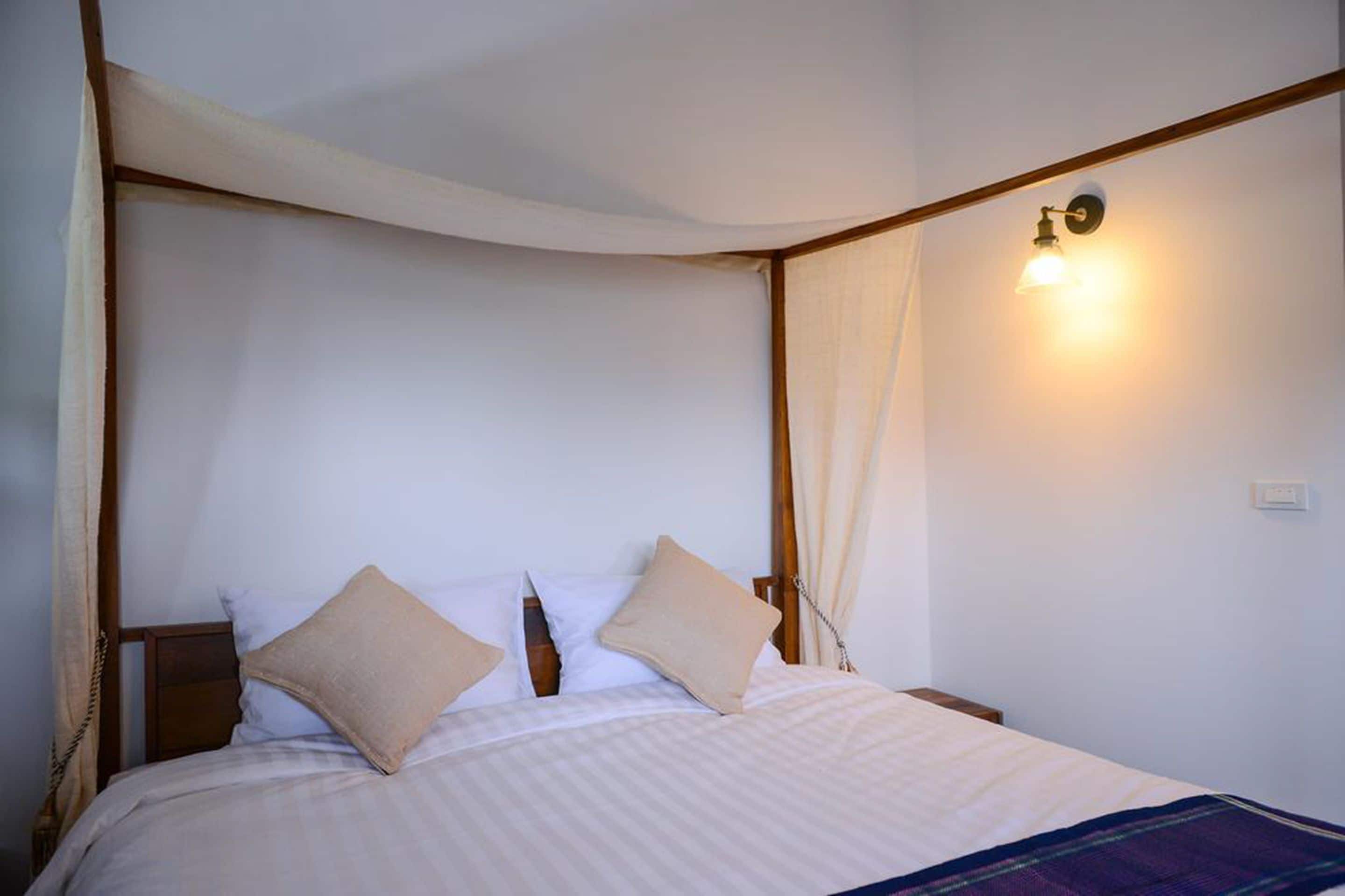 A bedroom with a four-poster bed, a bedside table, and a wall-mounted light fixture.