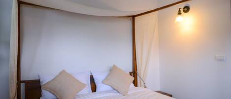 A bedroom with a four-poster bed, a bedside table, and a wall-mounted light fixture.