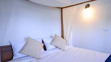 A neatly made bed with white bedding and beige pillows, a wooden headboard, and a wall-mounted light fixture.