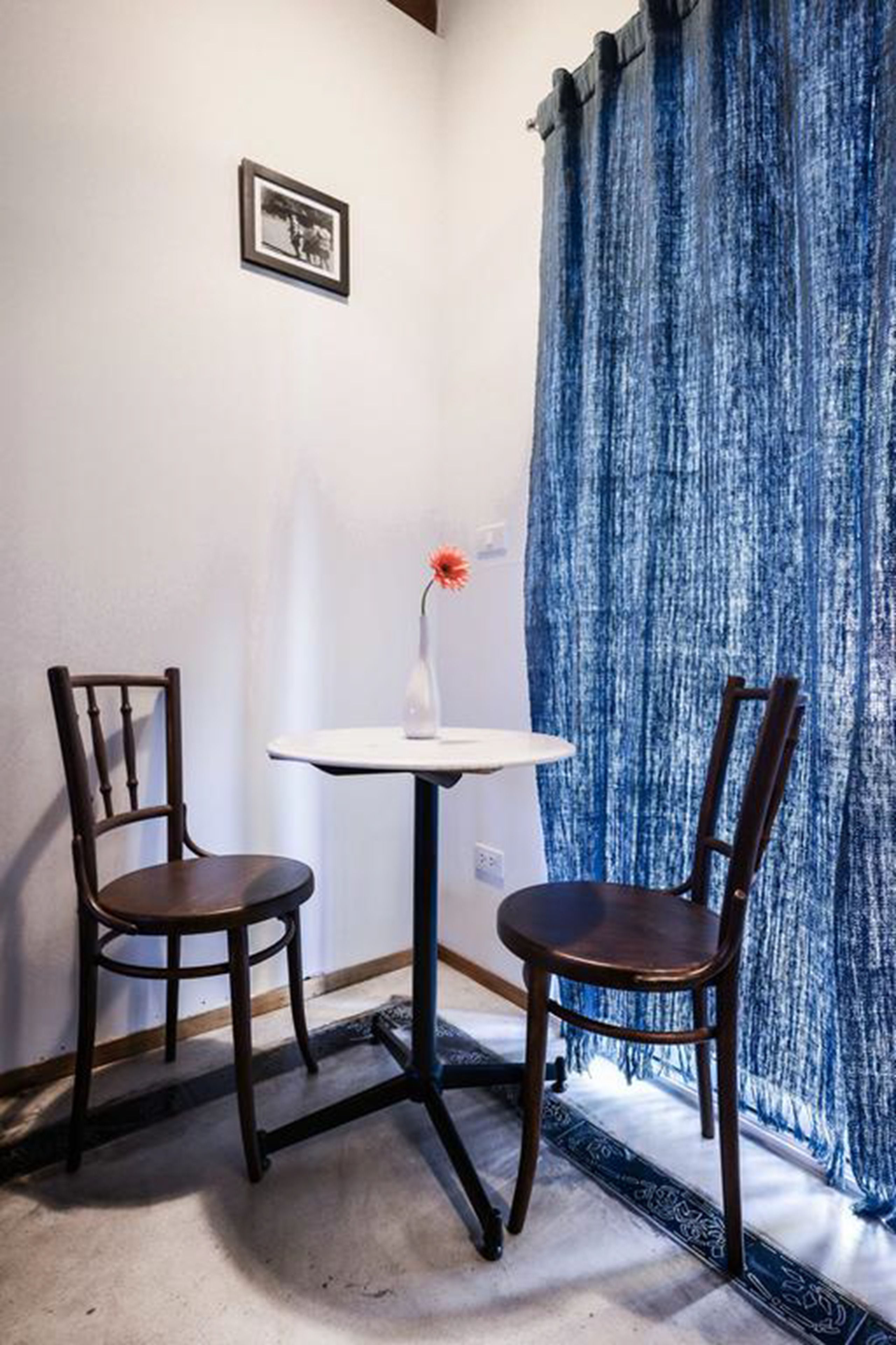 A corner room with two wooden chairs, a small white table, and a blue curtain.