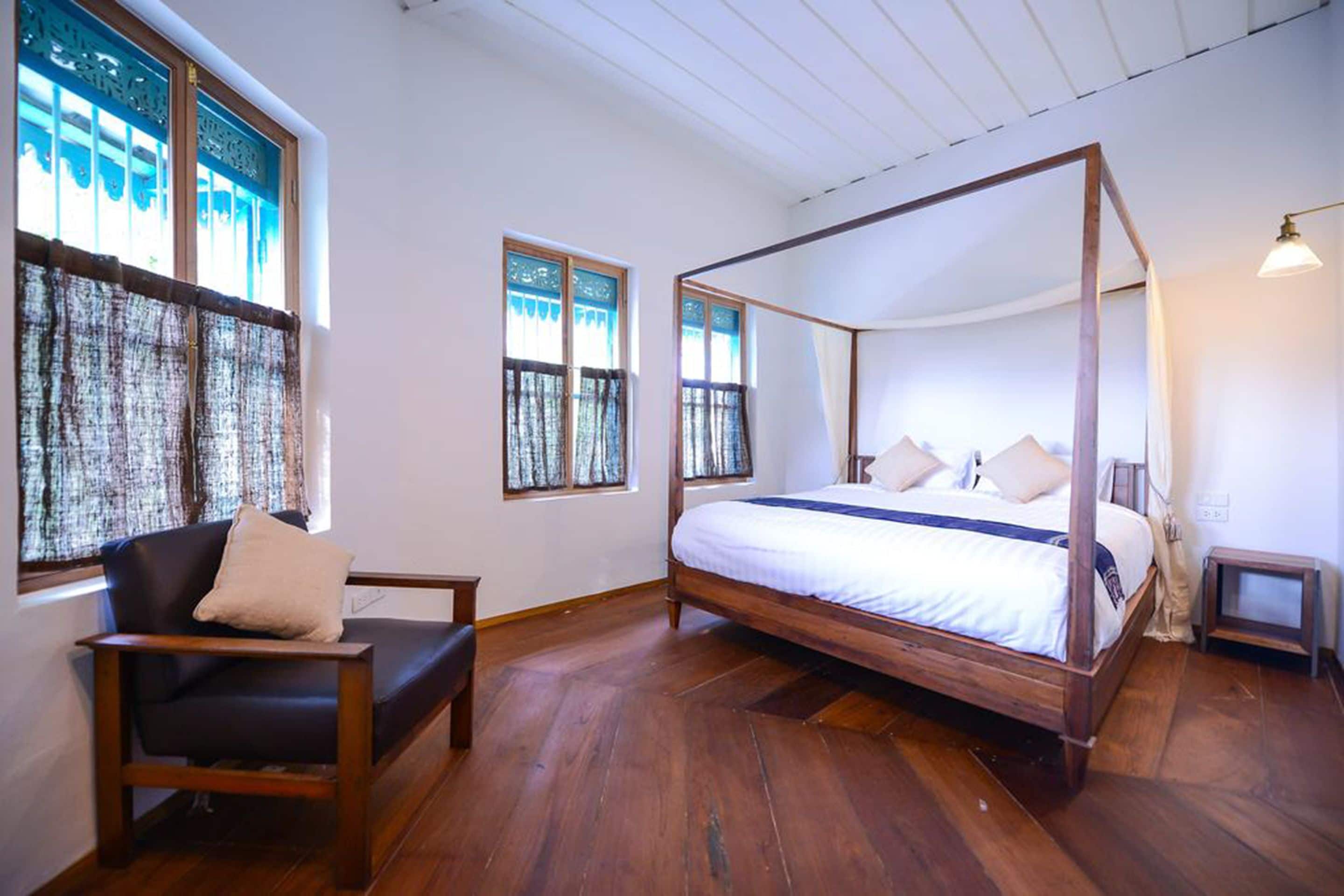 A four-poster bed with a wooden frame and white bedding, a dark leather sofa with a cushion, and a small wooden nightstand.