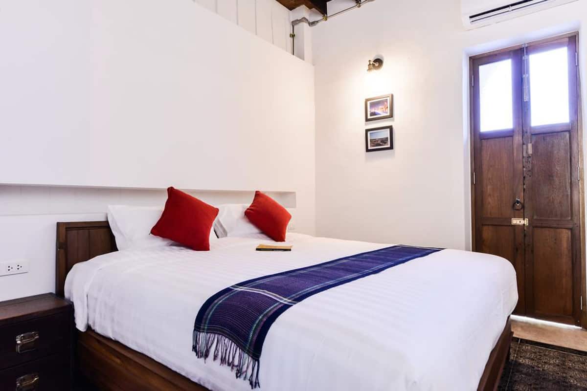 A neatly made bed with white bedding and red pillows, a wooden headboard, and a blue and white throw blanket.