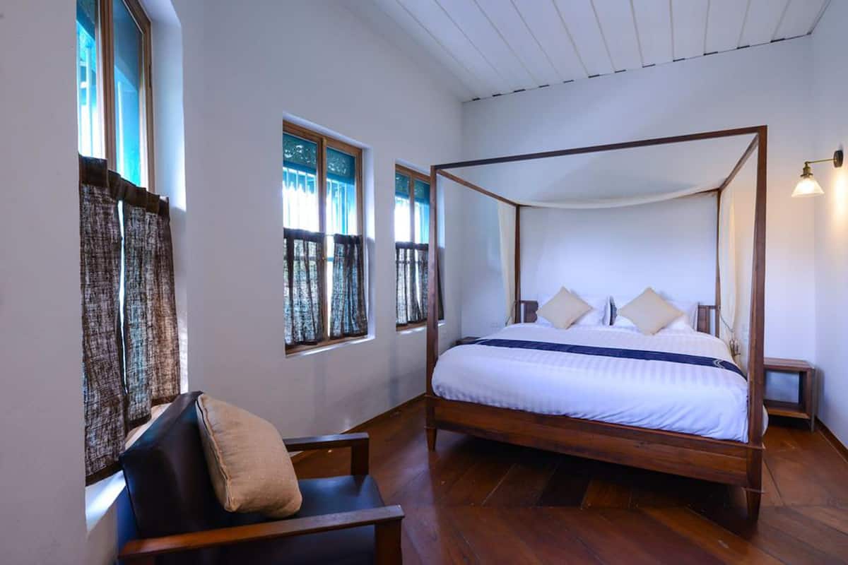 A four-poster bed with a canopy, a wooden chair, and a small bedside table.