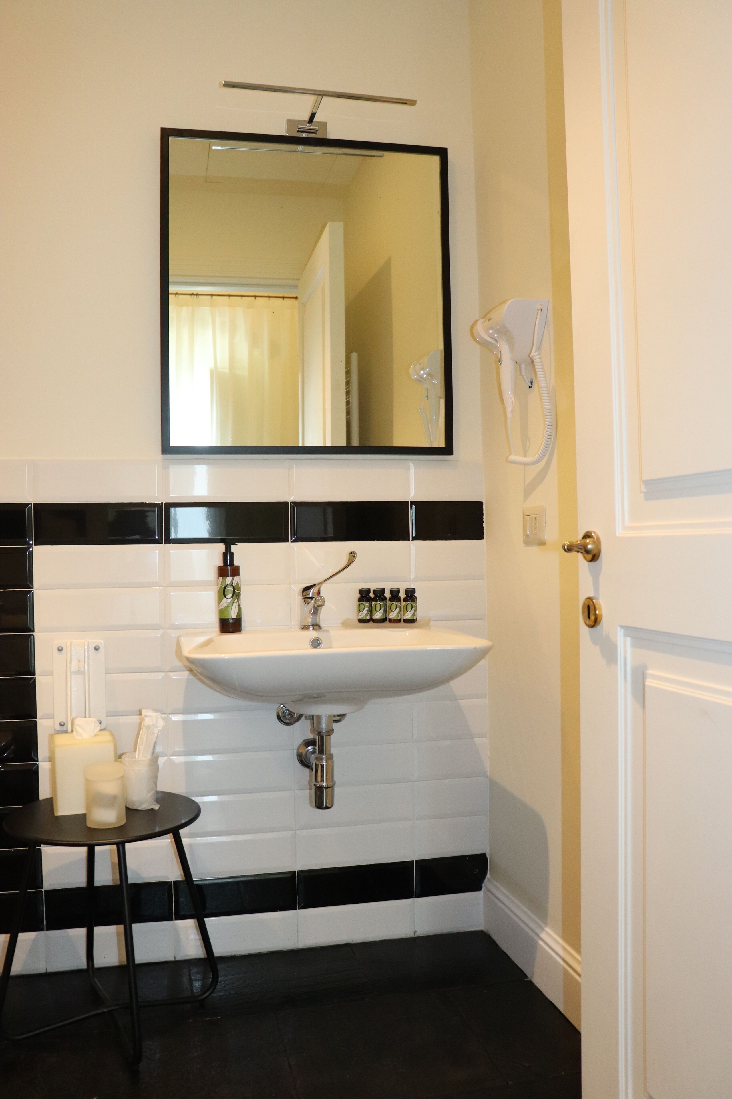 A bathroom with a white sink, black and white tiled walls, a mirror above the sink, and a door with a gold handle.