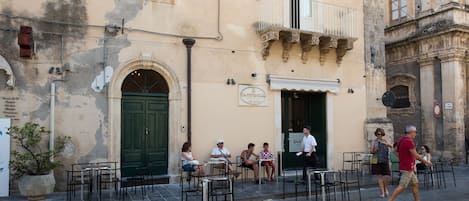 An outdoor café with outdoor seating, a green door, and a sign above the entrance.