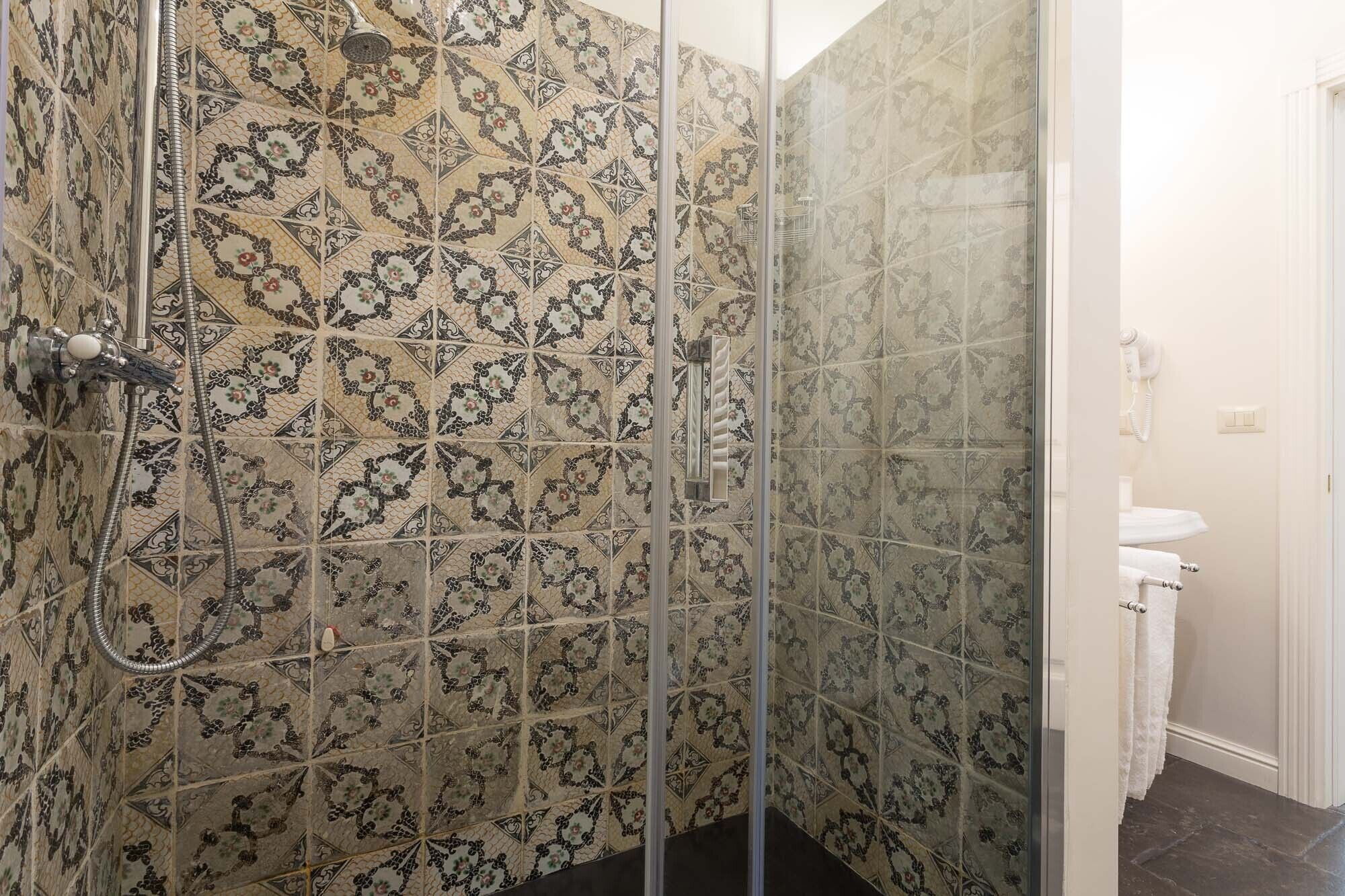 Eine Dusche mit gemusterten Fliesen und einer Glastür, neben einem weißen Waschbecken und einem Handtuchhalter.