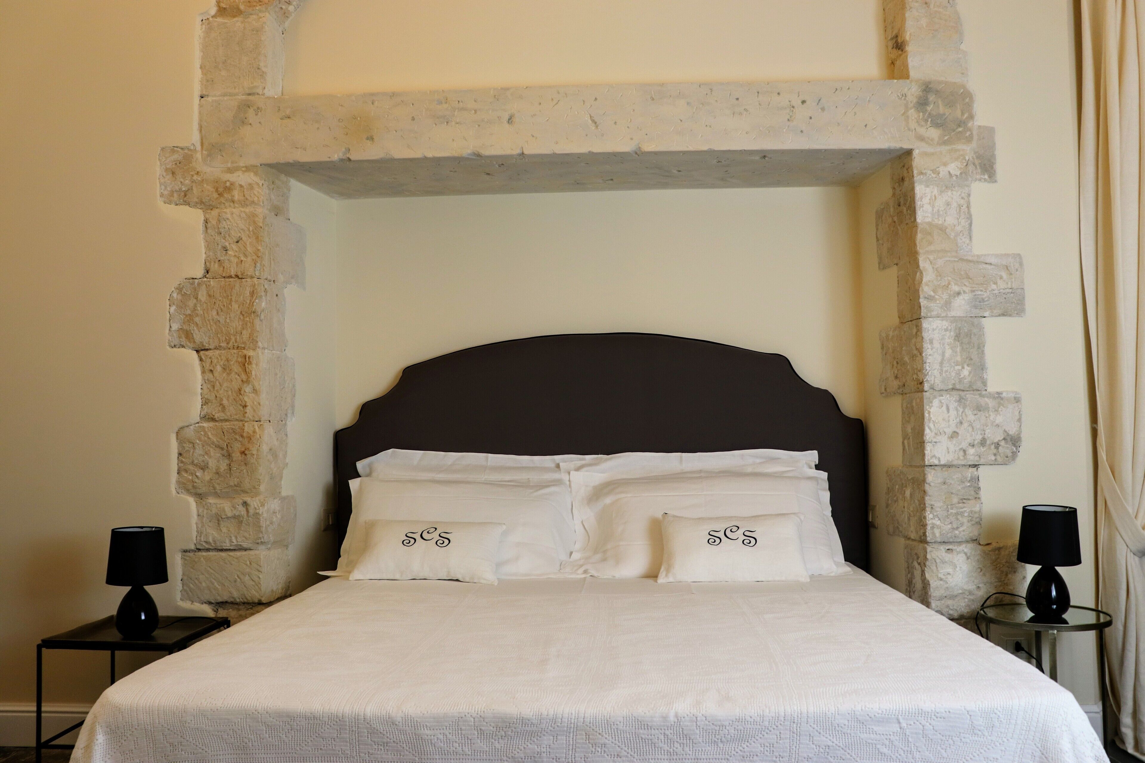 A bed with a stone headboard, white bedding, and two bedside tables with lamps.