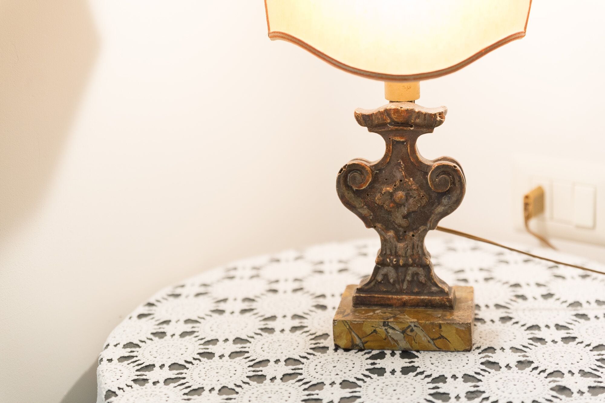 Una mesa con mantel de encaje y una lámpara ornamentada con luz encendida.