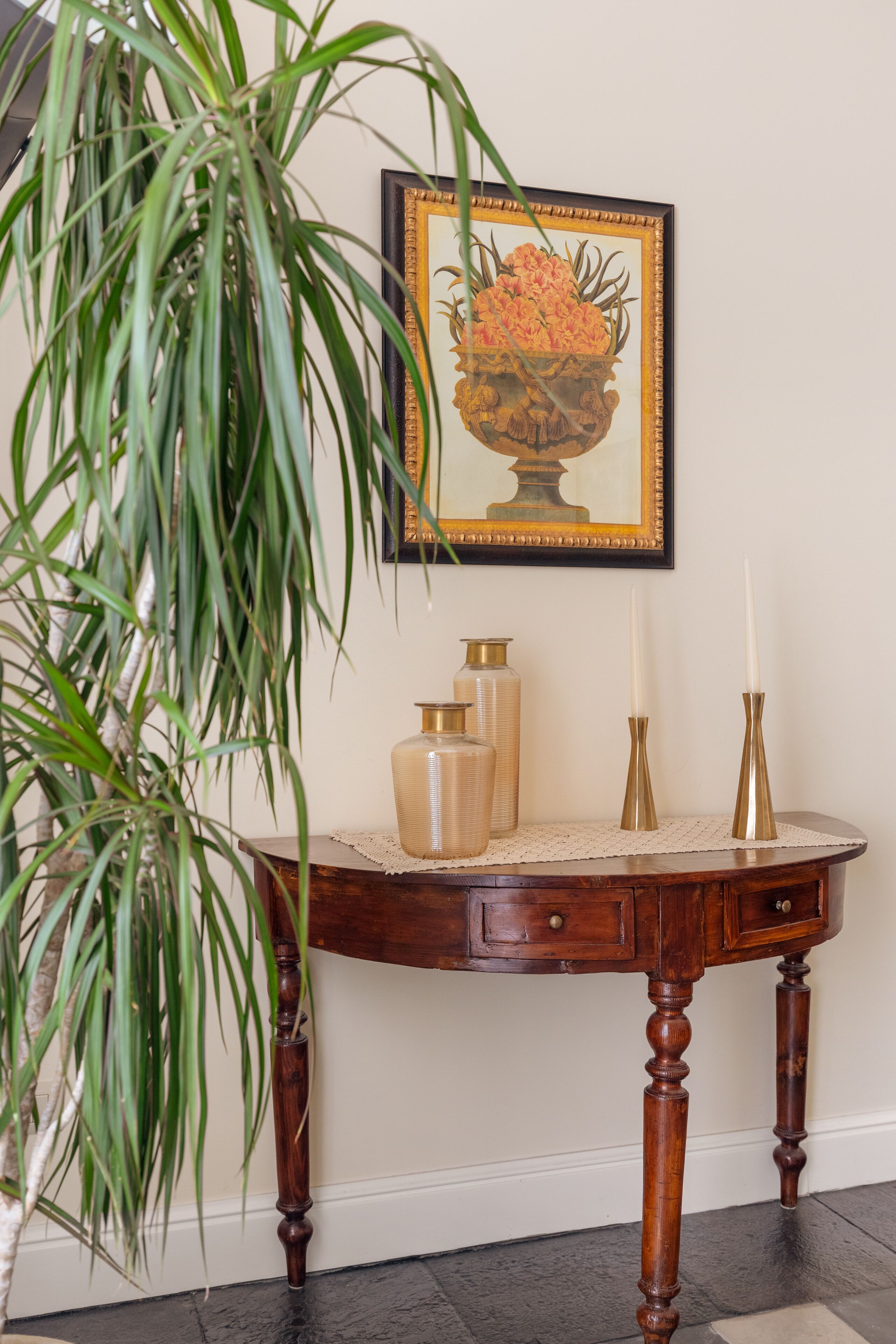 A wooden table with a vase, candle holders, and a framed painting on the wall.