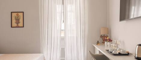 Ein Hotelzimmer mit einem Bett, einem Schreibtisch mit Frühstücksgedecke, einem Stuhl und einem großen Fenster mit durchsichtigen Vorhängen.