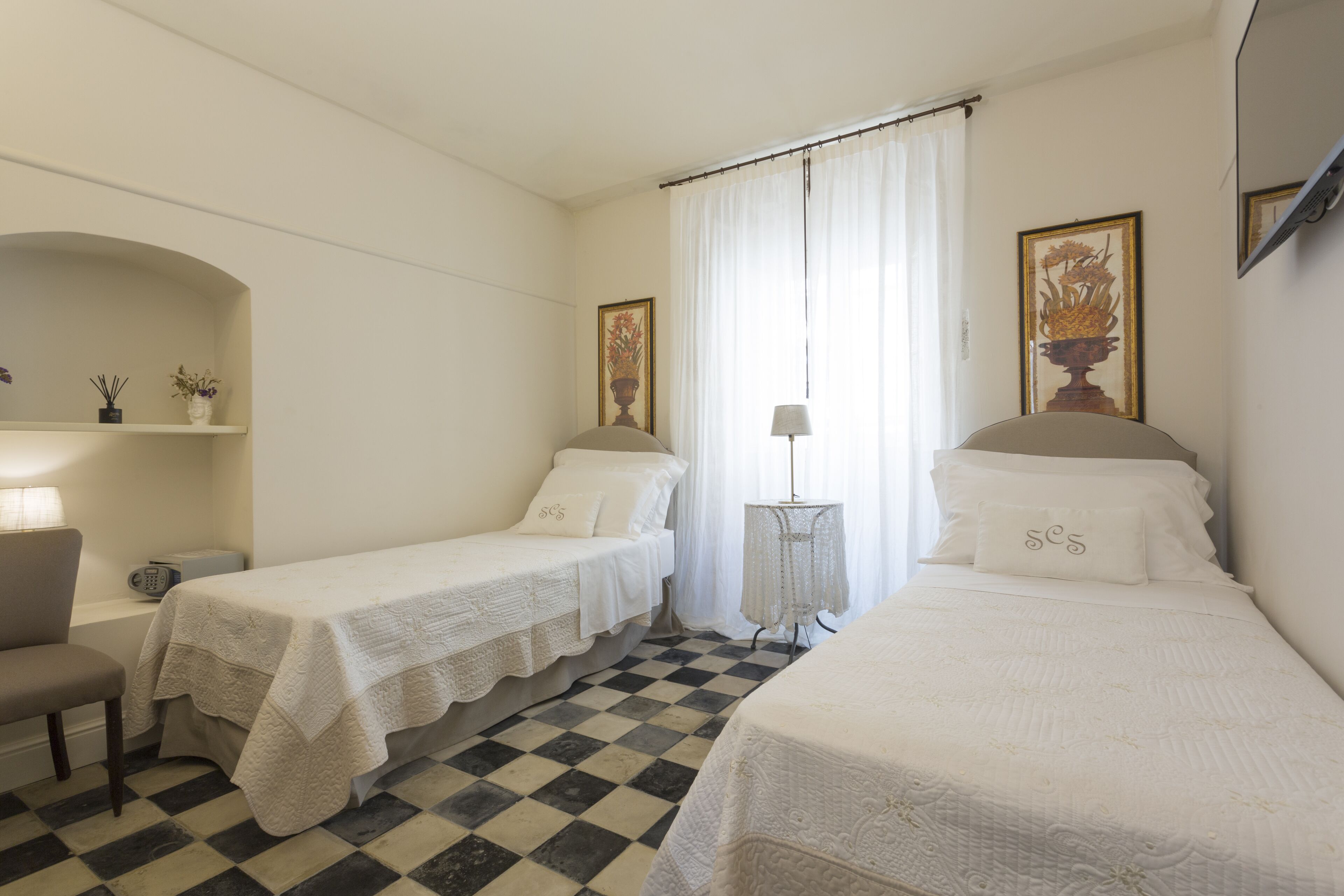 A hotel room with two single beds, a chair, a small table, and a lamp.