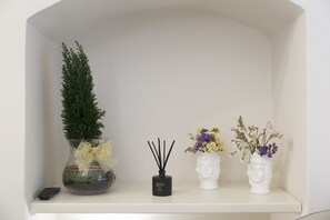 A shelf with a potted plant, a black diffuser, and two vases with flowers. - San Carlo Suites (Noto)