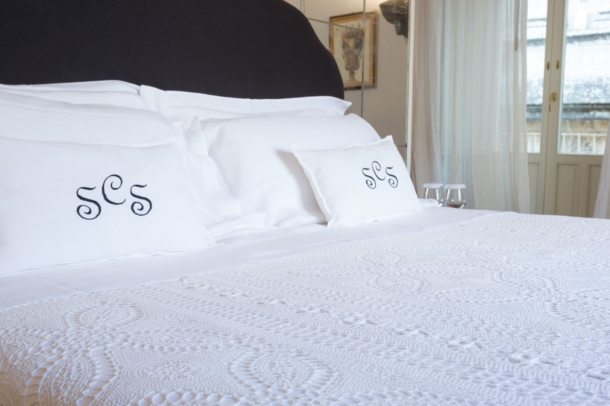 A neatly made bed with white linens and pillows, each with a monogrammed design.