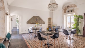 A dining area with tables and chairs, a chandelier, and a patterned floor. - San Carlo Suites (Noto)