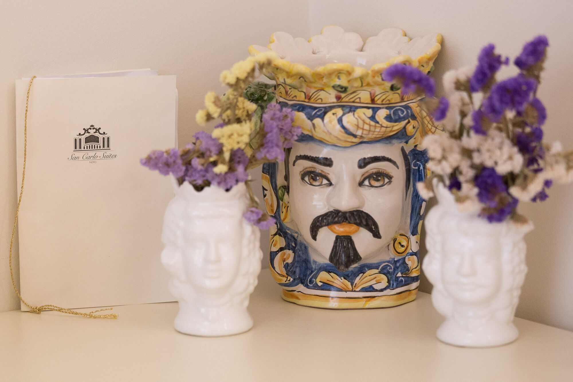 Un jarrón de cerámica decorativo con arreglos florales, un sobre blanco y un logotipo.