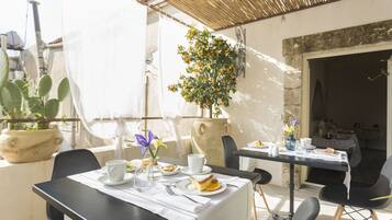Un coin repas avec une table dressée pour deux personnes, une plante en pot et une vue sur la rue.