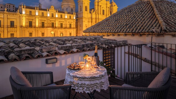 A terrace with a table set for dining, overlooking a historic building with domed architecture. - San Carlo Suites (Noto)