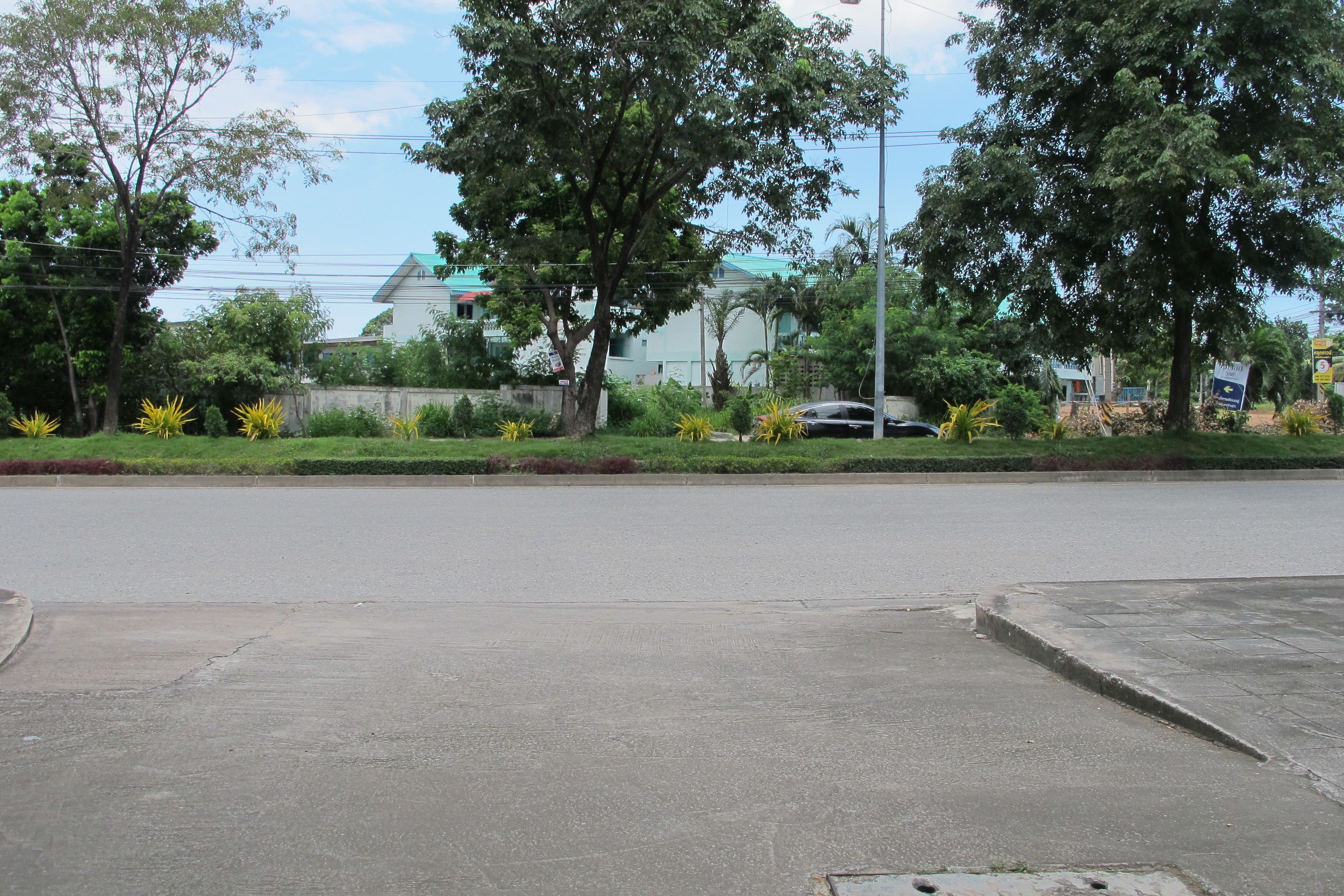 A street with a sidewalk, trees, and a building in the background.