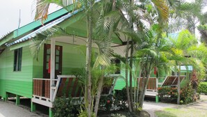 A green building with a porch, surrounded by palm trees and plants. - The Green Resort Sri Racha (Si Racha)