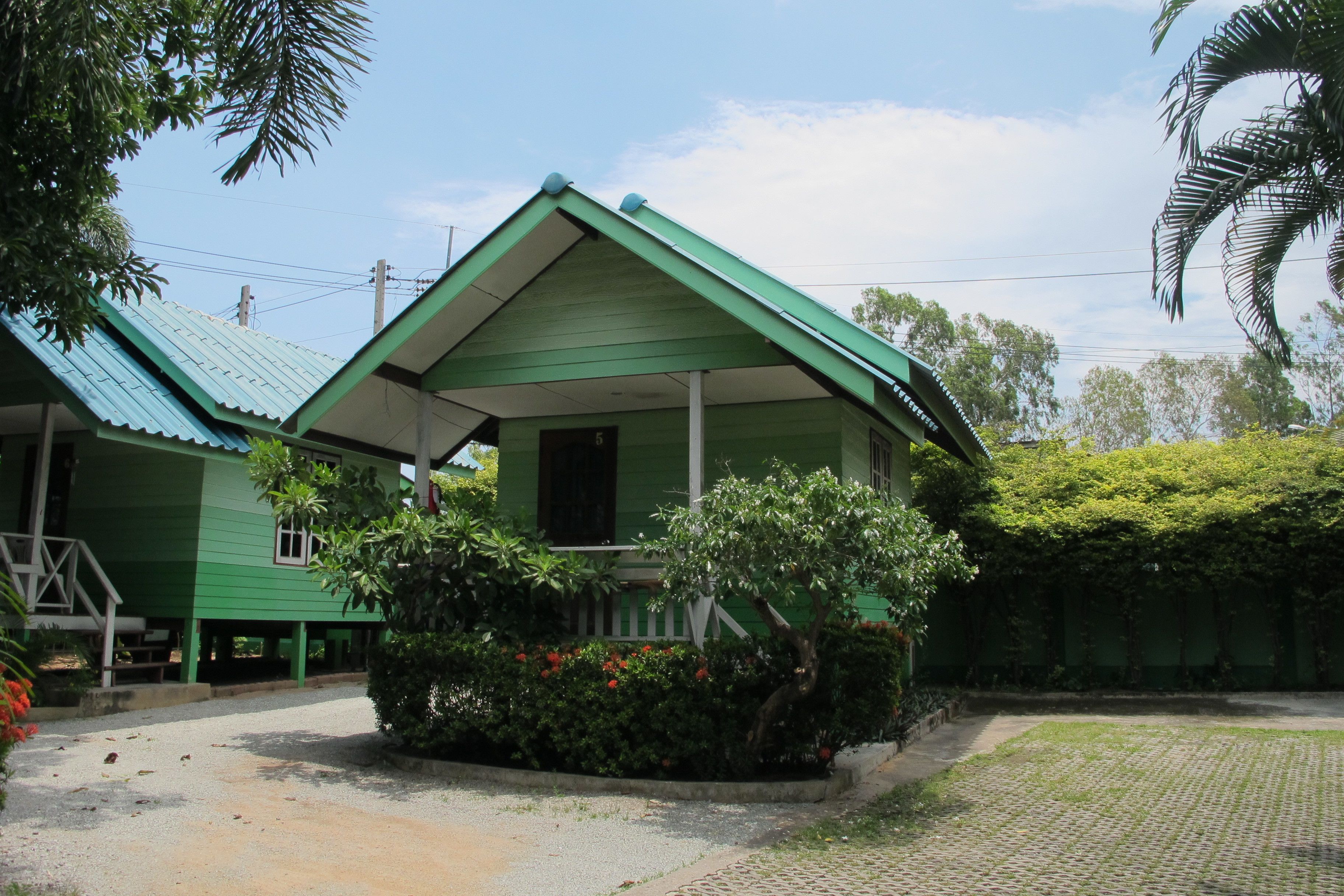 A green building with a sloped roof, a porch, and a garden area with red flowers.