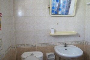 Casa de banho com sanita, bidé, lavatório e uma prateleira com rolo de papel higiénico.