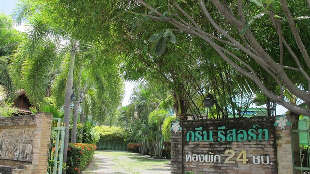 A sign with Thai text indicating a location, surrounded by lush greenery and a paved path. - The Green Resort Sri Racha (Si Racha)