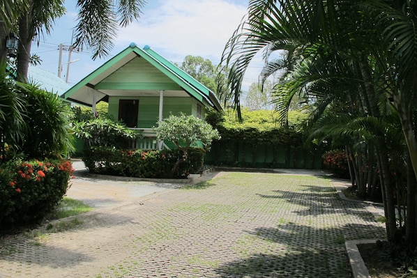 Um edifício verde com varanda, rodeado por vegetação exuberante e um caminho de pedras.