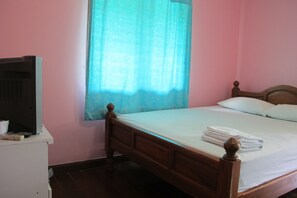 Quarto com cama de madeira, mesa de cabeceira branca, televisão sobre um móvel e janela com cortina azul.