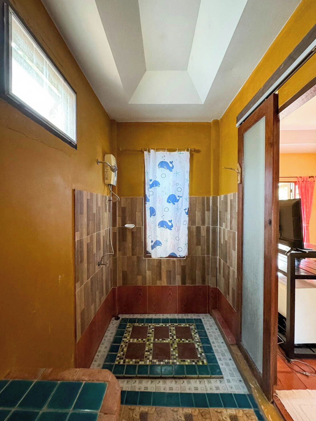 A small, enclosed shower area with a tiled floor, a showerhead, and a curtain with a whale pattern.