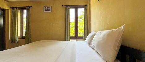 A large bed with white linens in a room with yellow walls and two windows with curtains.