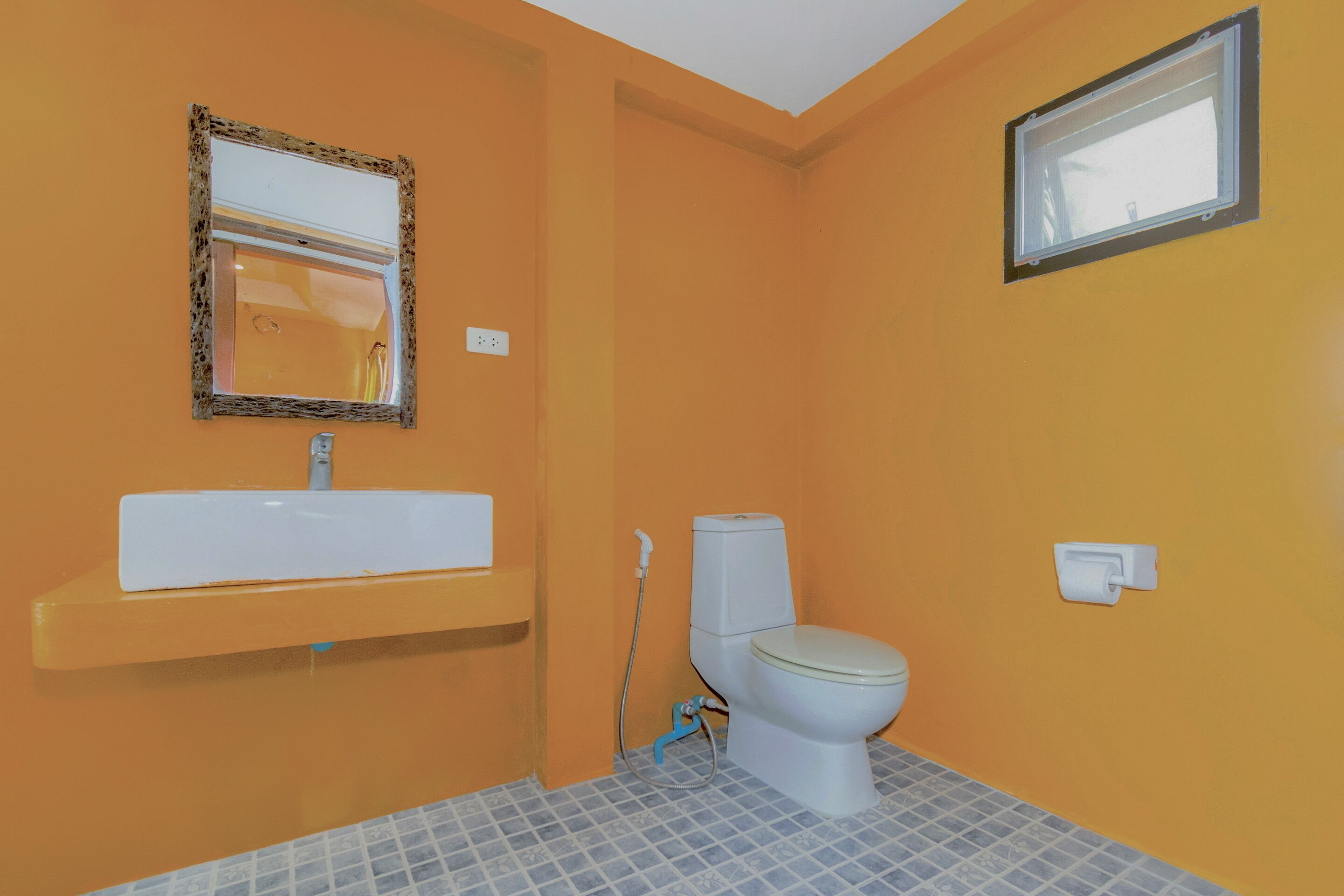 A bathroom with an orange wall, a white sink, a toilet, and a window.