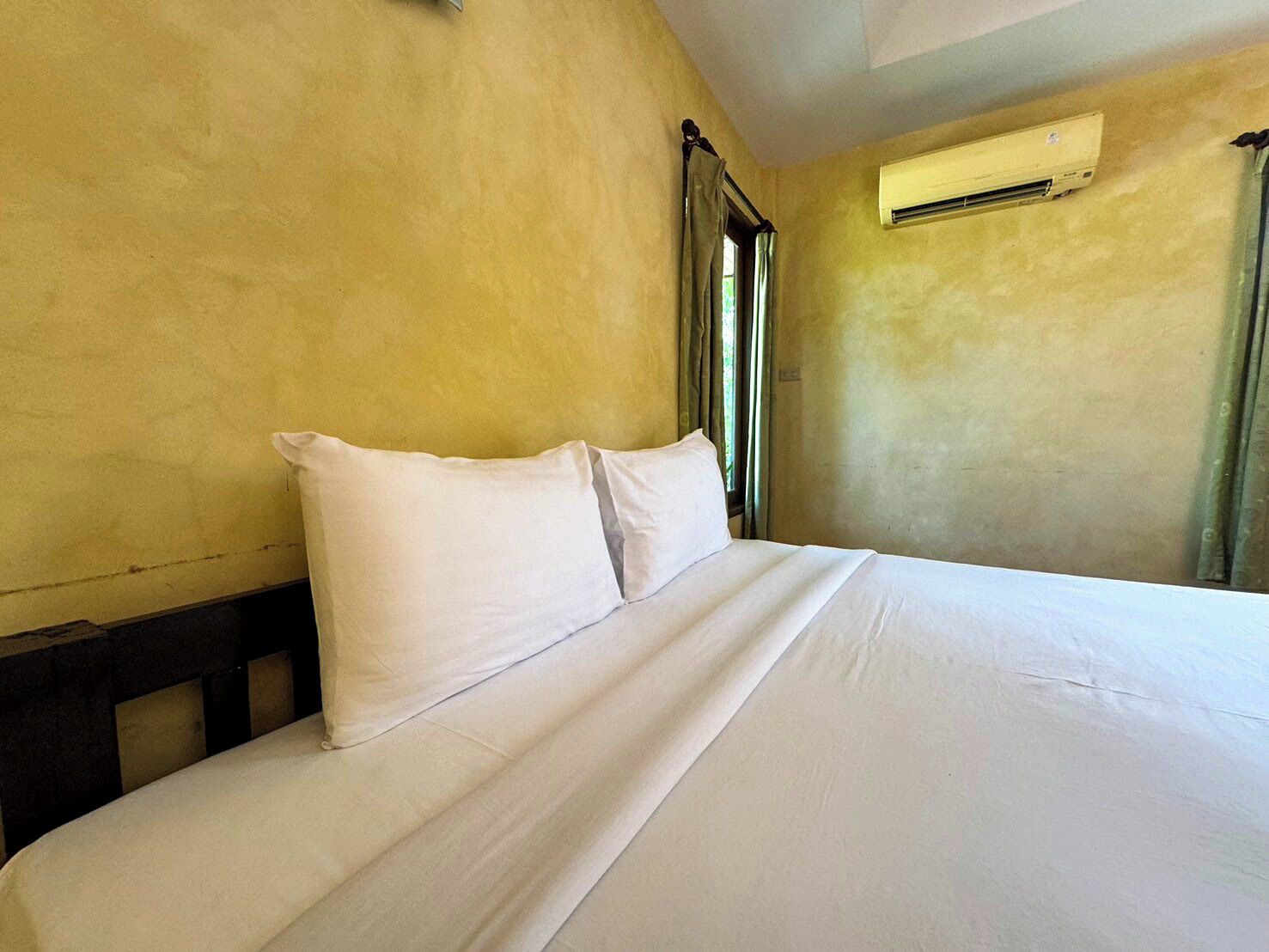 A hotel room with a bed, a window with curtains, and an air conditioning unit on the wall.