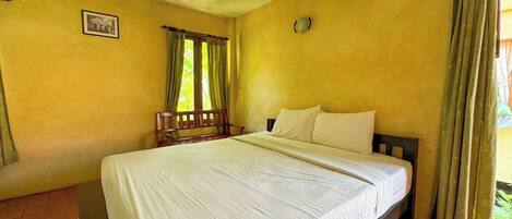 A bedroom with a large bed, a wooden bench, a window with curtains, and a wall clock.