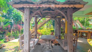 A wooden gazebo with a table and benches, surrounded by lush greenery and a brick pathway. - Baanbali Beach Resort (Pranburi)