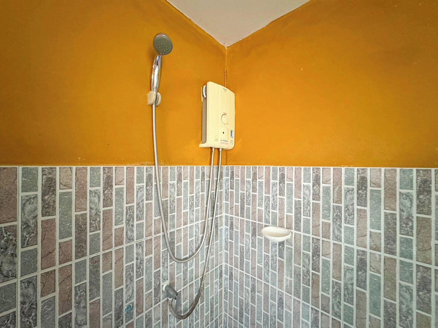 A corner shower with a handheld showerhead and a wall-mounted control box.