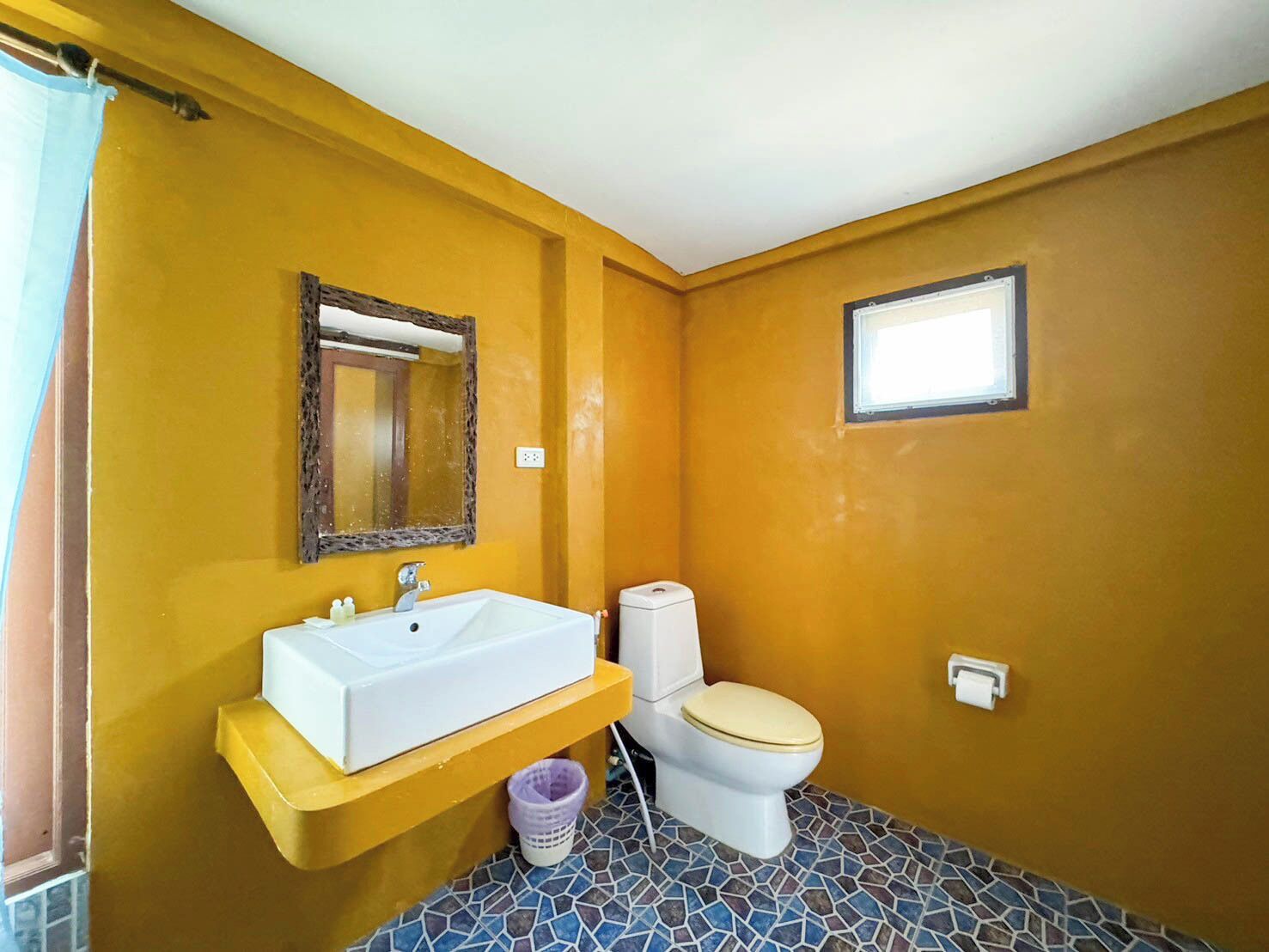 A bathroom with a yellow wall, a white sink, a toilet, and a small window.